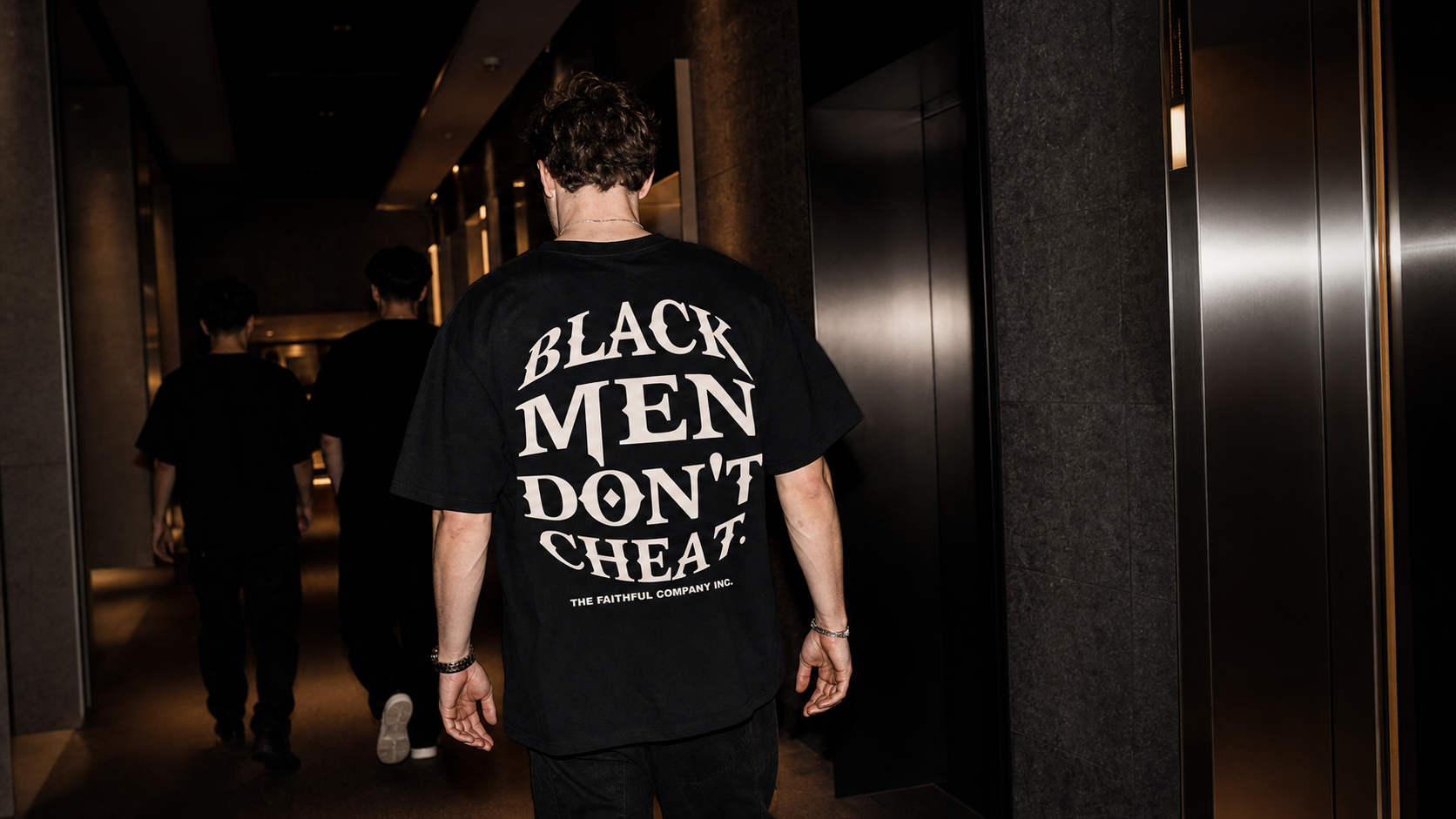Back view of the Debut Tee in a dark Tokyo hotel corridor
